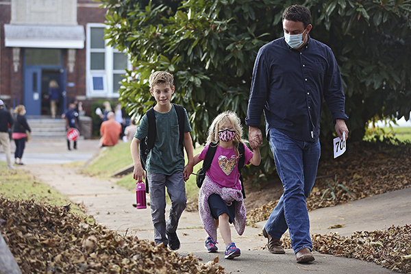 Wes Holmes, right, walks with is daughter Hollace Holmes after her first day of pre-kindergarten at Council Oak Elementary School in Tulsa, Okla., Monday, Nov. 9, 2020. Tulsa Public School returned to in-person instruction for kindergartners and pre-kindergartners on Monday, amid the coronavirus pandemic. At left is Dawson Holmes, 8, his son and Hollace's brother. (Mike Simons/Tulsa World via AP)