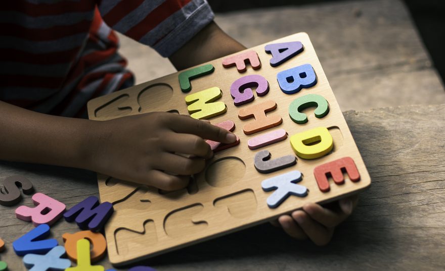 English alphabet made of square wooden blocks. The child's hand grabs the alphabet to put it in the correct block.