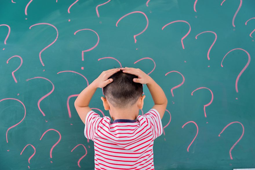 Asian little boy in front of blackboard with question marks.
